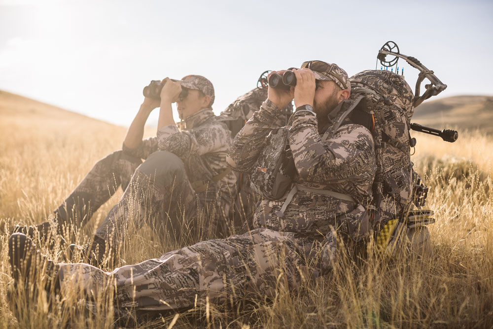 Hunters sit in a field in Sitka gear