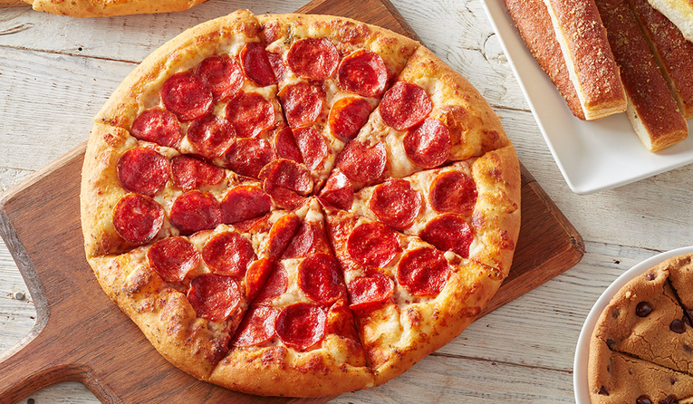 pepperoni pizza on a wooden board with breadsticks and a chocolate chip cookie