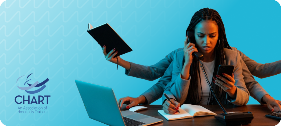 Woman multitasking at a desk, holding a phone, notebook, and pen, with a focused expression. Laptop and documents on the table. Blue background with CHART logo.
